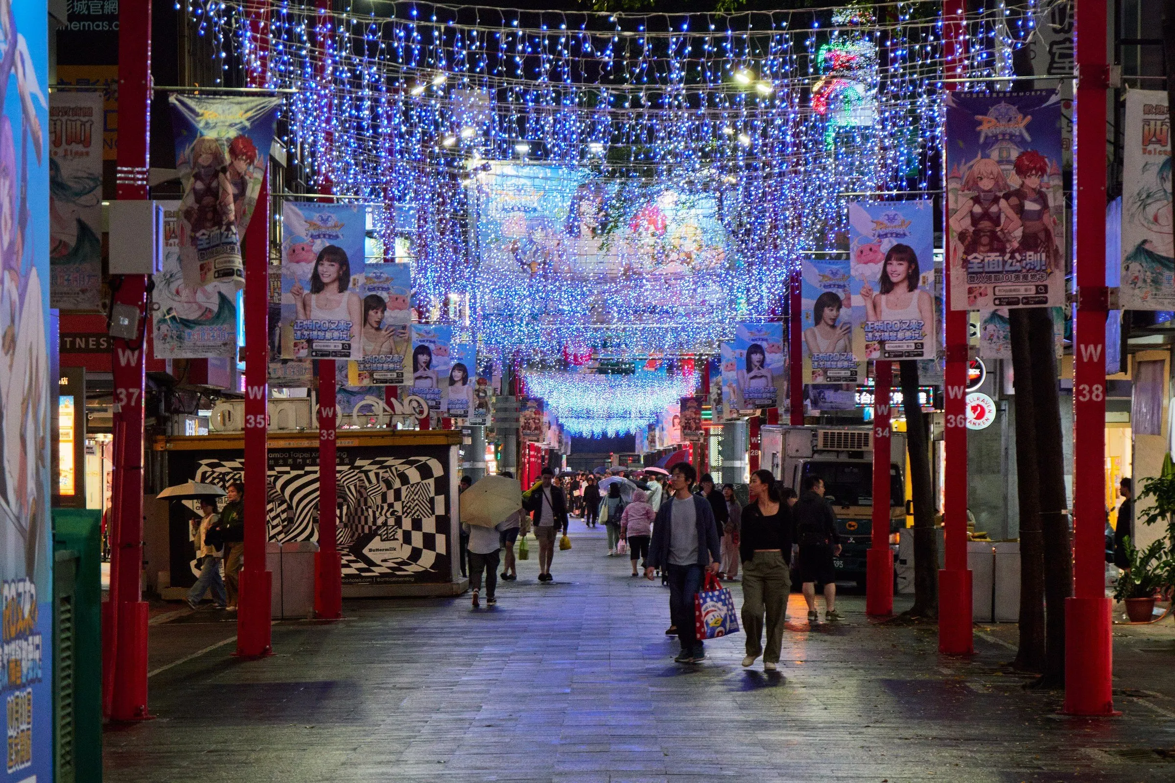 Rua de pedestres de Ximending à noite, com luzes azuis suspensas, anúncios e pessoas caminhando.