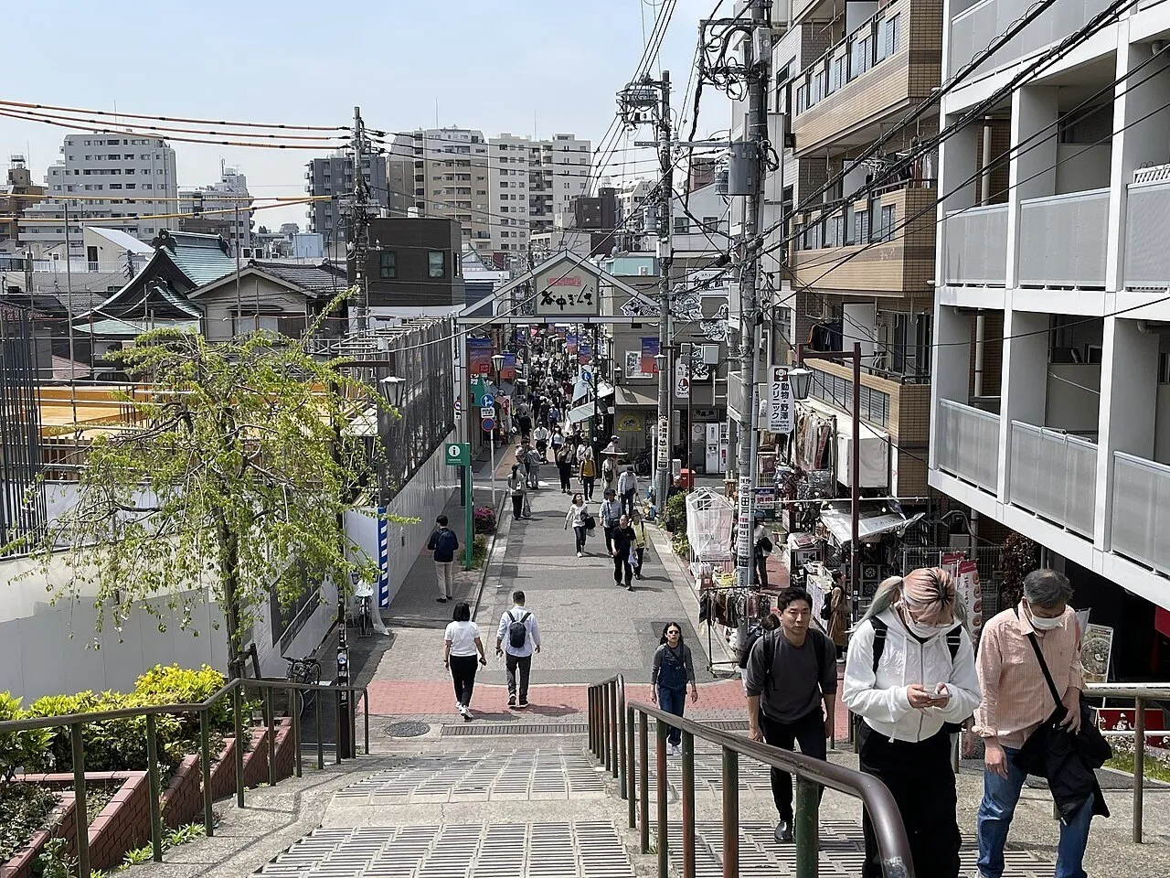 Yanaka Ginza vista do alto da escadaria, com lojas, pórtico e pedestres distribuídos pela rua.