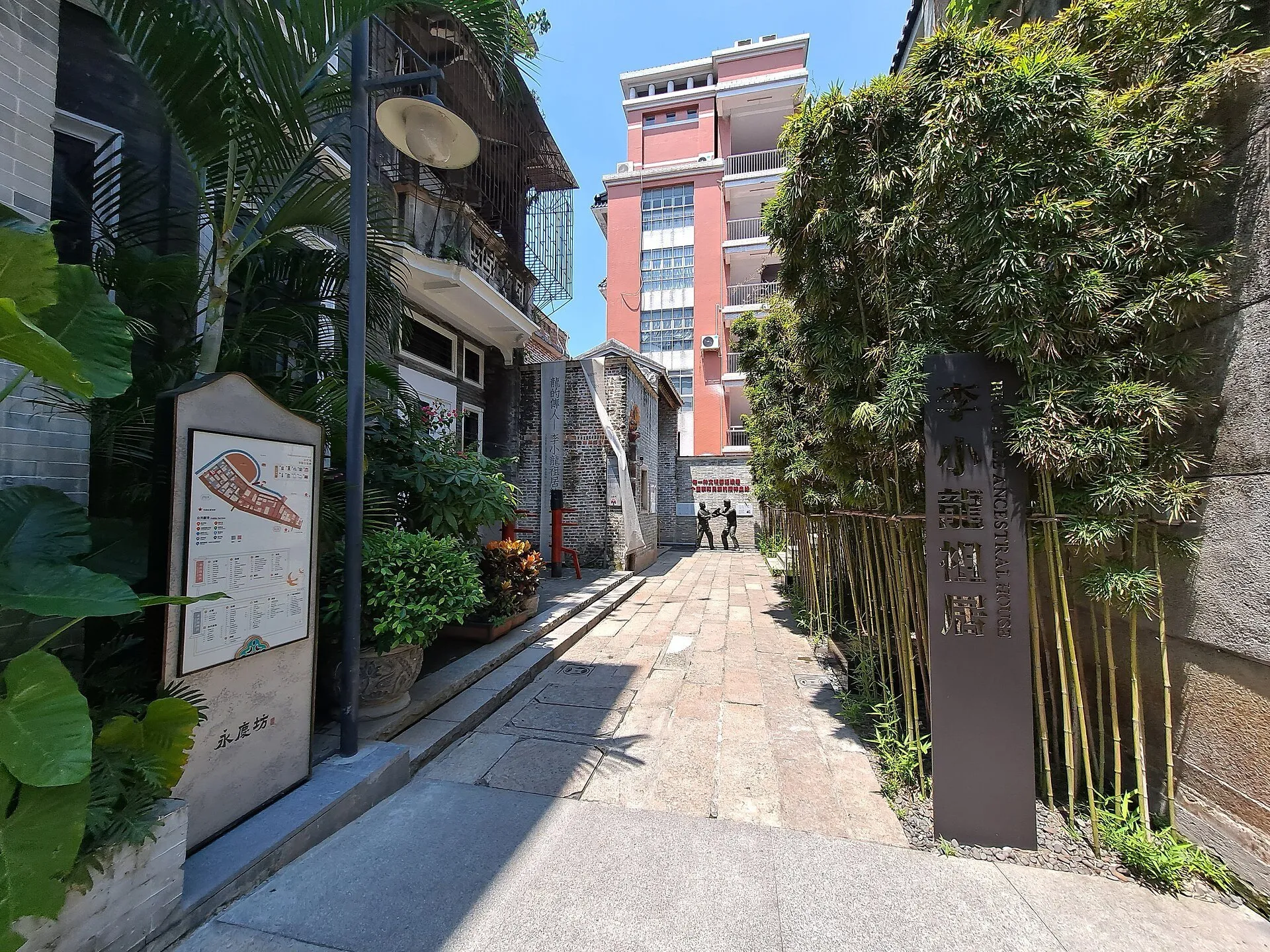 Viela de Yongqing Fang com casas, bambus, placas e uma fachada rosada ao fundo.